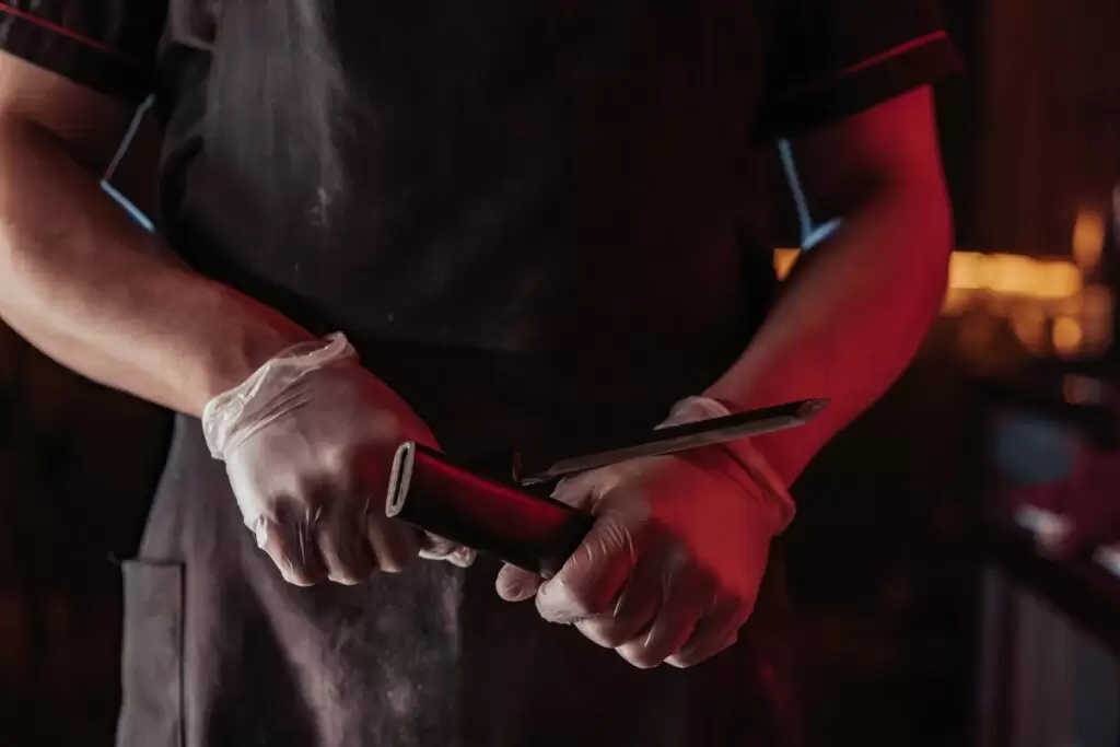 Man wearing chef apron and gloves preparing to sharpen a knife.